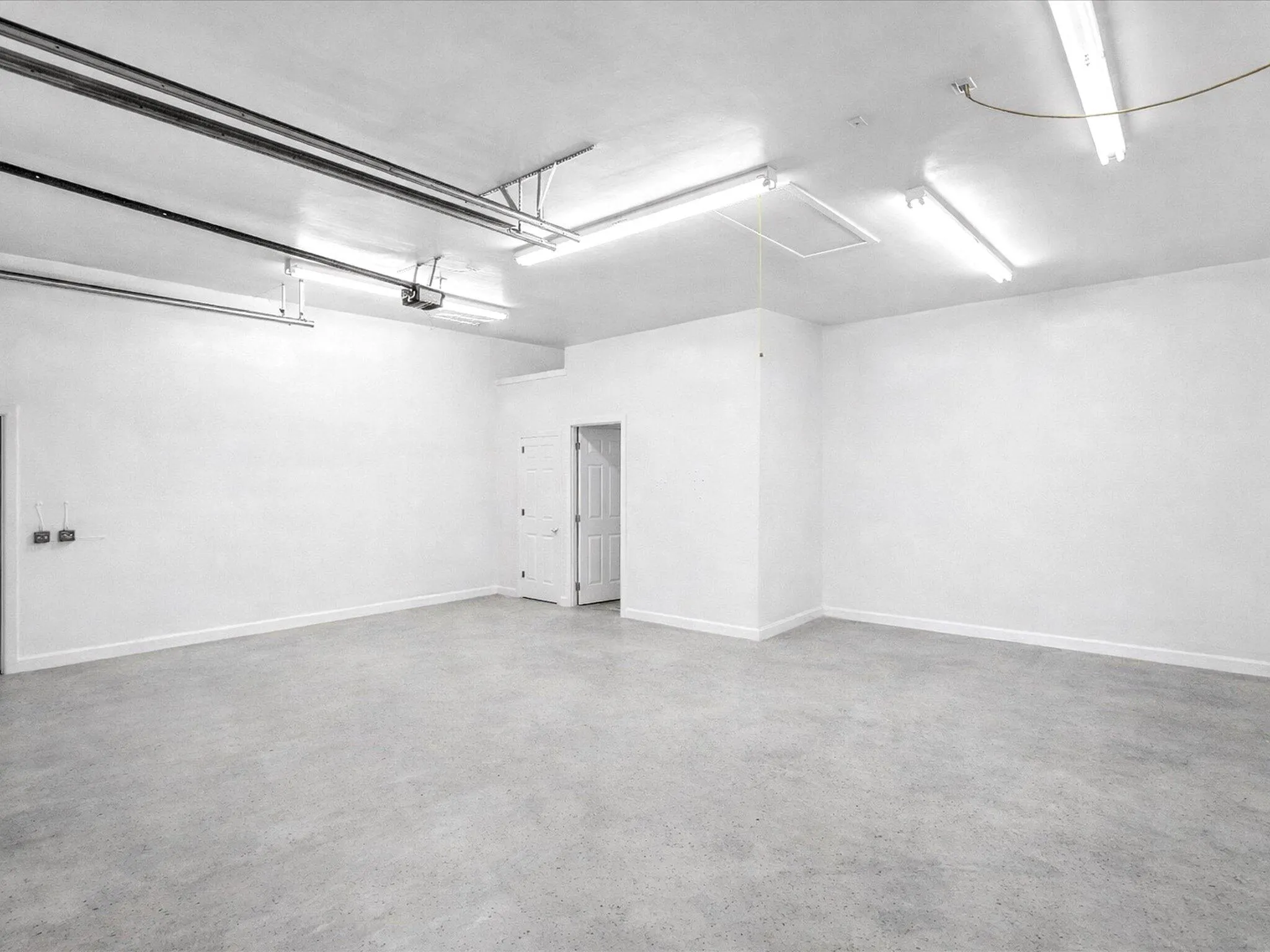 Spacious garage with concrete flooring, multiple fluorescent light fixtures, and a white interior door