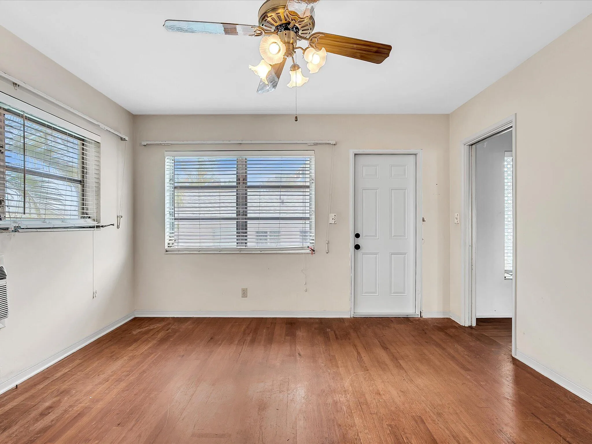 Wood-finish flooring throughout, two windows with blinds, ceiling fan with light fixture, and a white paneled door