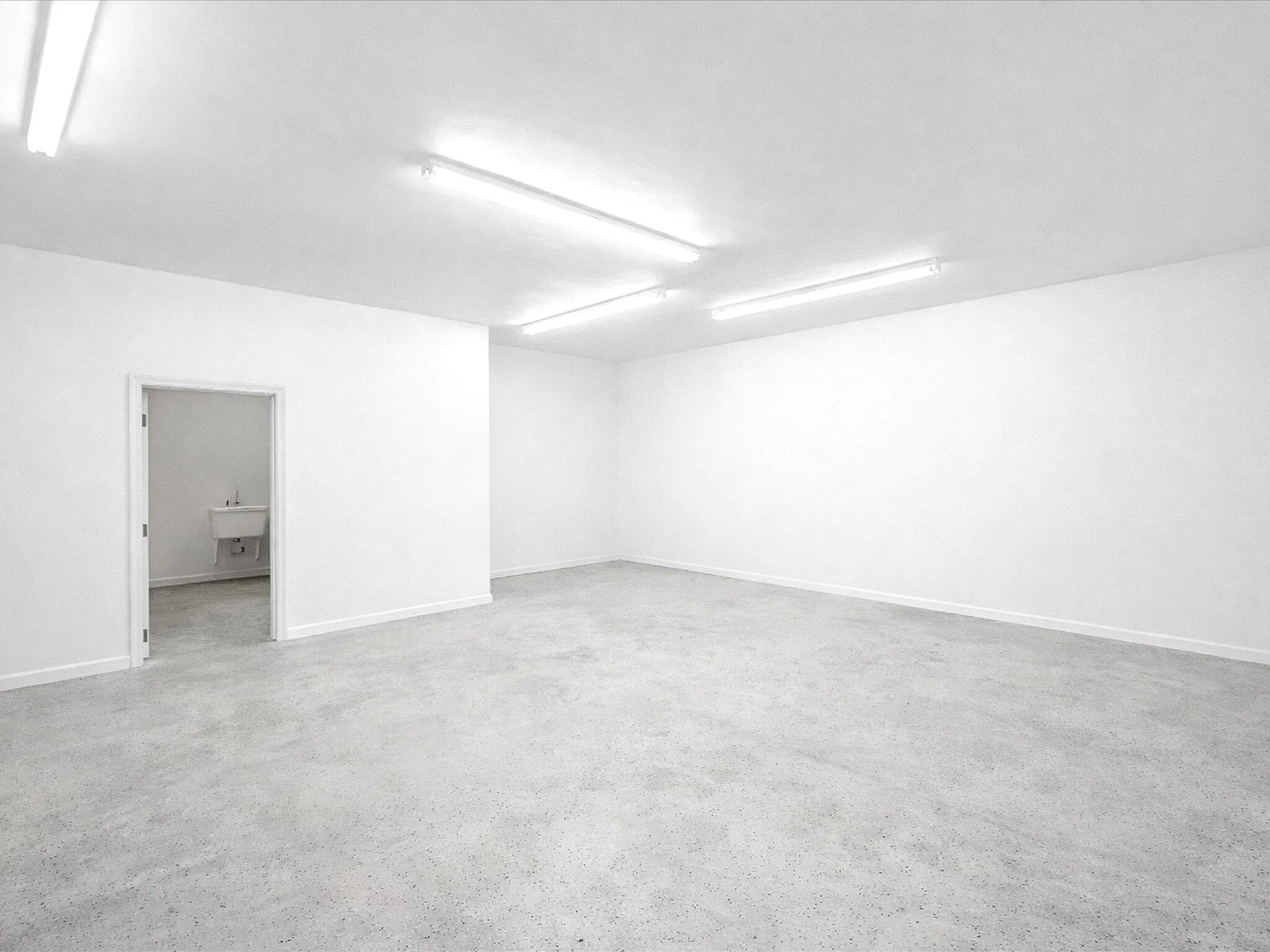 Spacious room with concrete flooring, white walls, and overhead fluorescent lighting