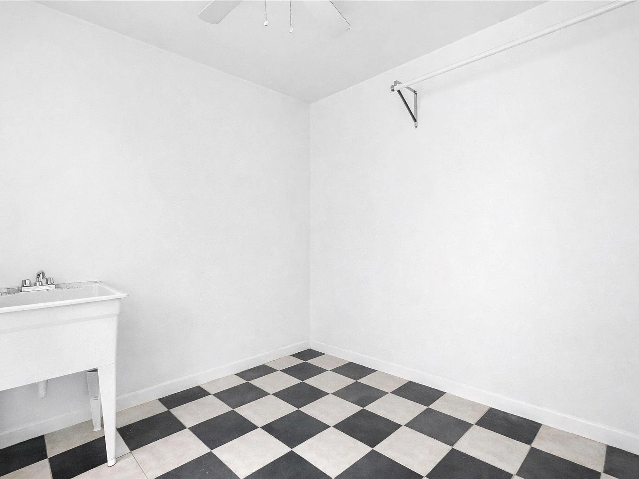 White utility sink, checkerboard flooring, ceiling-mounted fan, and wall-mounted drying rod