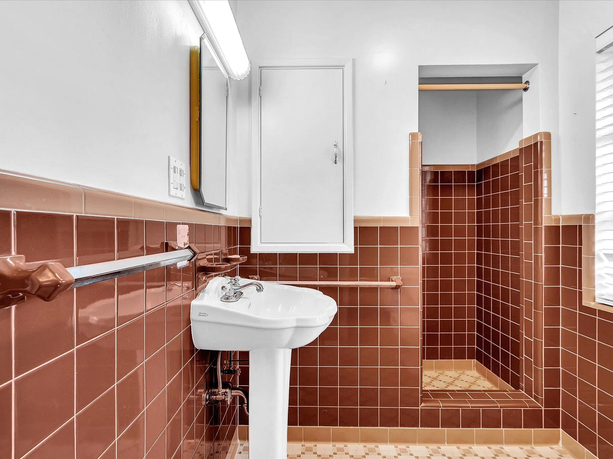 Pedestal sink, wall-mounted medicine cabinet, brown tiled walls, tiled shower stall, and patterned tile flooring