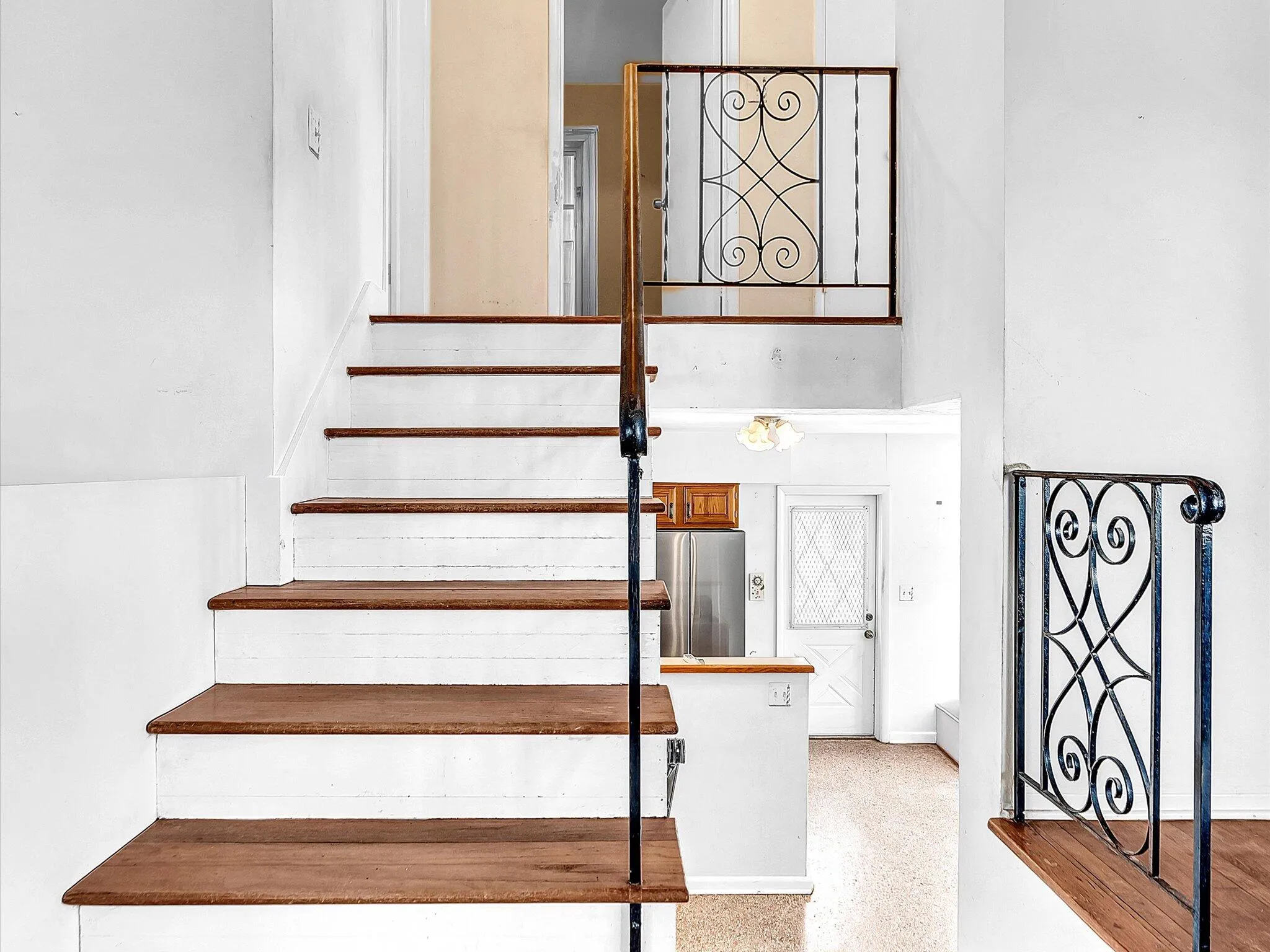 Staircase featuring wood-finish treads and risers, with decorative wrought iron railings