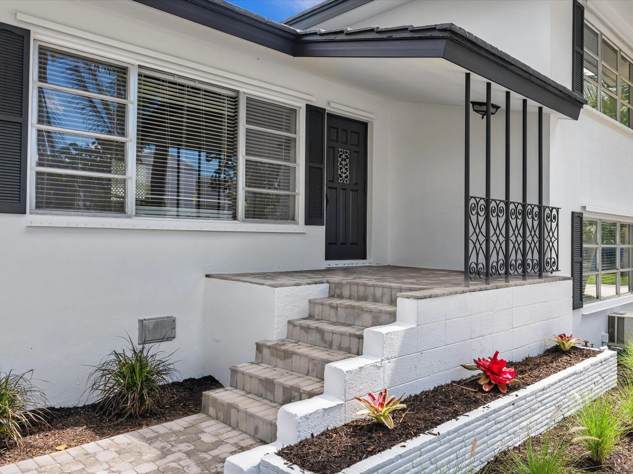 Front entry featuring an ornate wrought iron railing, brick paver steps, and a covered porch