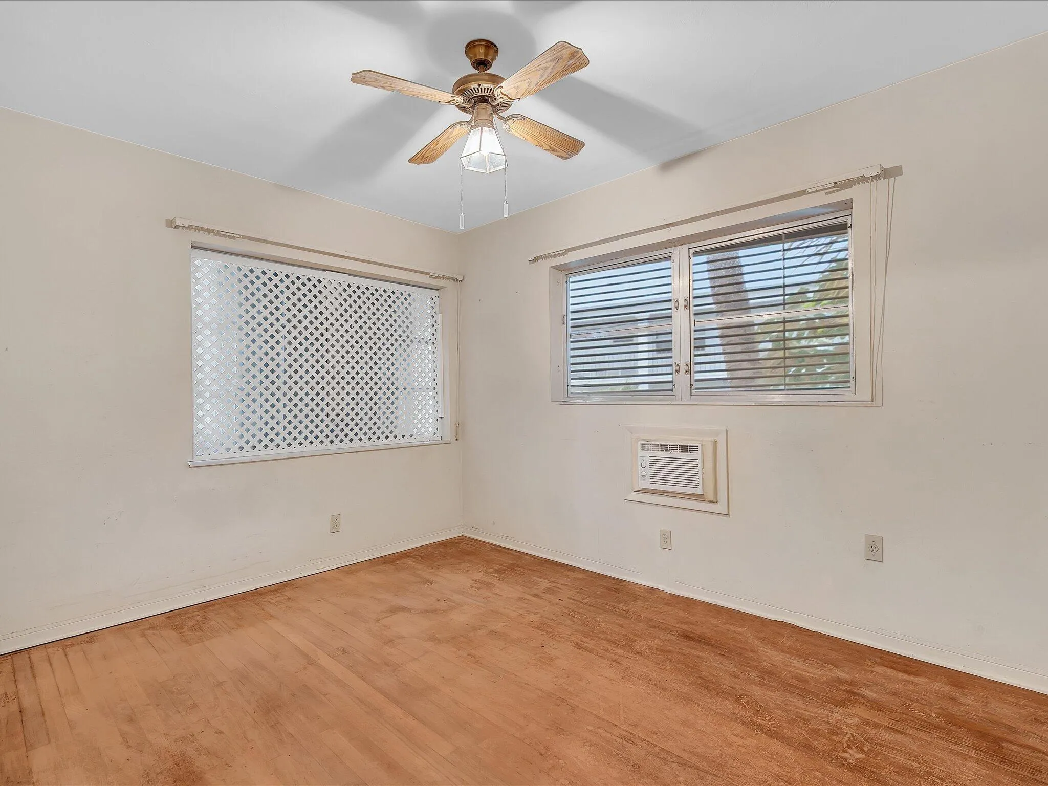Wood-finish flooring with white walls, two windows with blinds, and a ceiling fan with integrated lighting