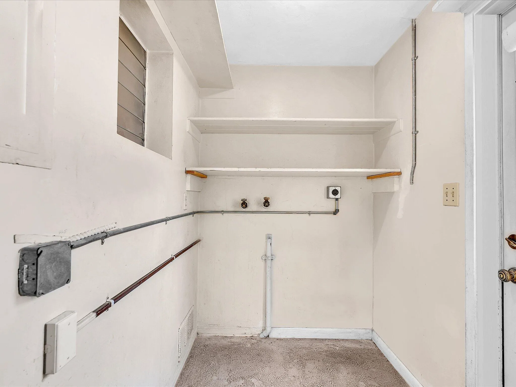 Utility space featuring two wall-mounted shelves, a louvered window, and exposed conduit