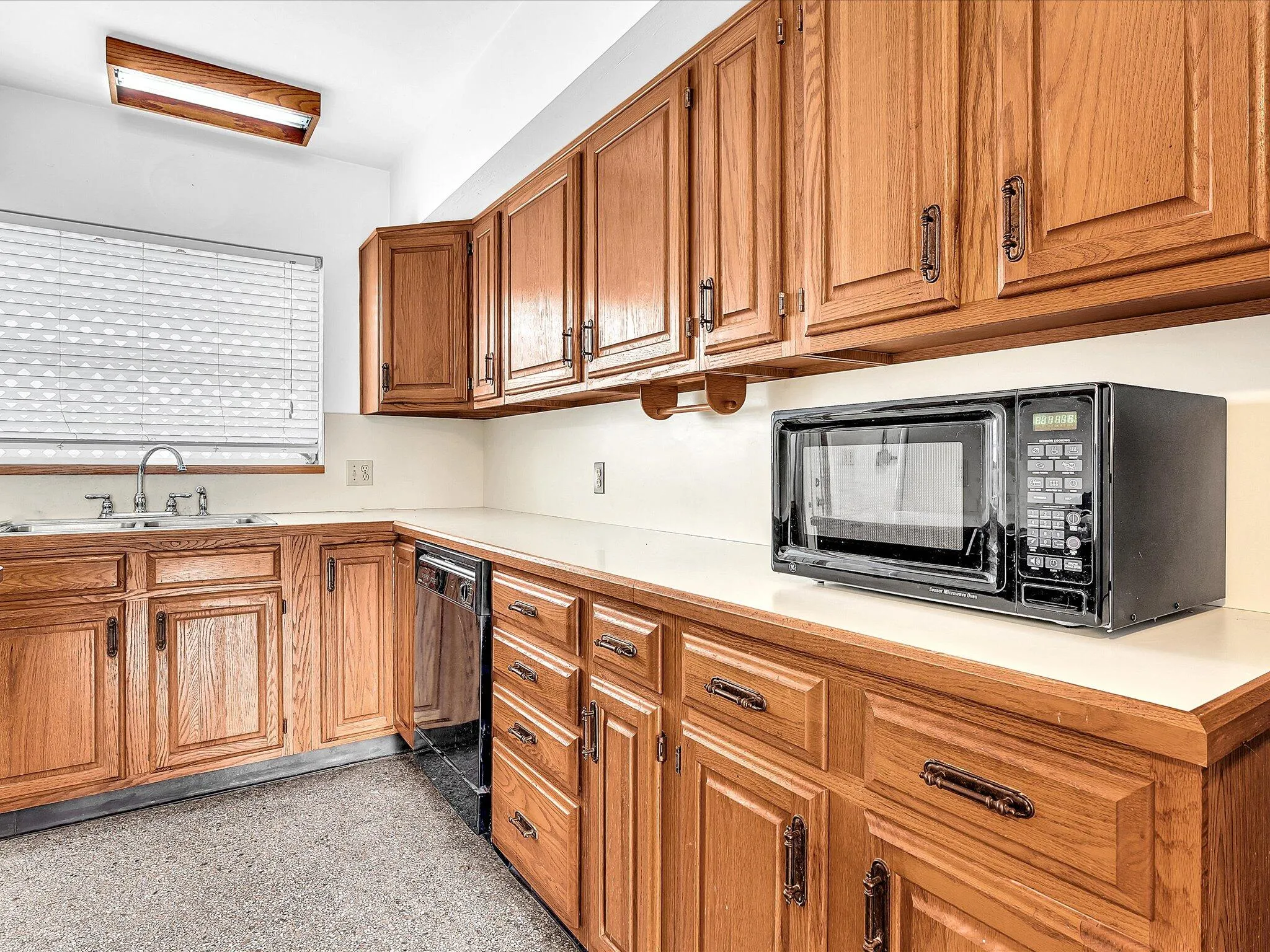 L-shaped kitchen featuring wood cabinetry, solid surface countertops, stainless steel sink, and durable flooring