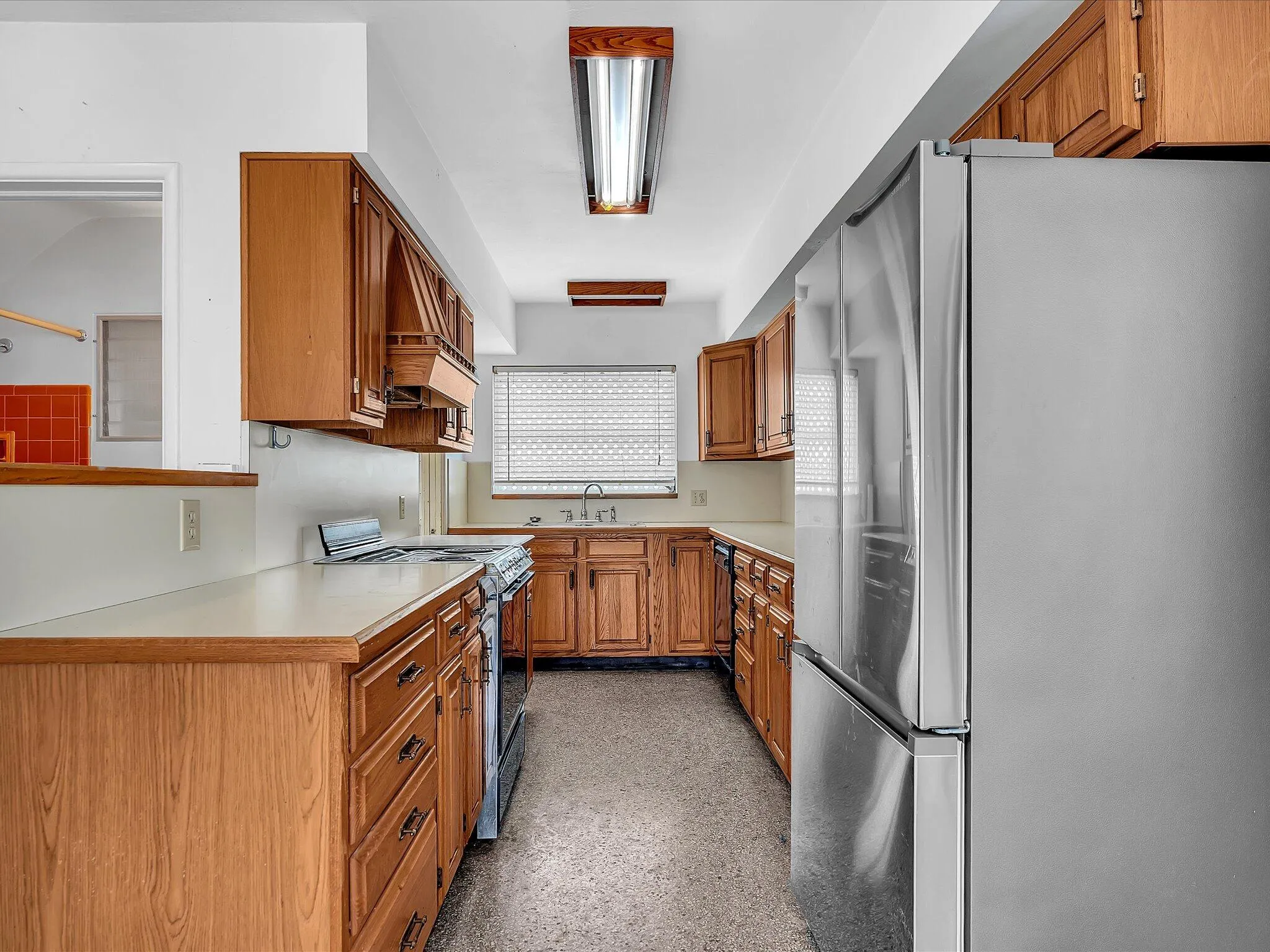 Galley kitchen featuring wood cabinetry, light-toned countertops, and stainless steel appliances