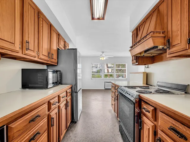 Galley kitchen with wood-finish cabinetry, white countertops, built-in electric range, and a stainless steel refrigerator