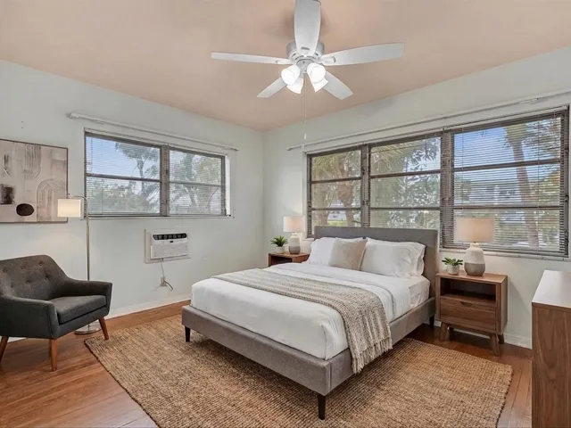 Hardwood-finish flooring, multiple windows with blinds, ceiling fan with light fixture, wall-mounted air conditioning unit