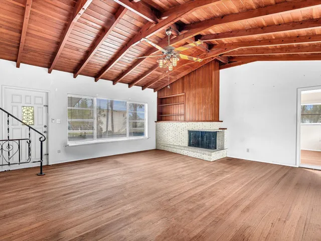 Vaulted wood-paneled ceiling, wood-finish flooring, built-in fireplace with brick surround, built-in shelving, and multiple windows