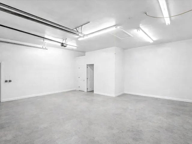 Spacious garage with concrete flooring, multiple fluorescent light fixtures, and a white interior door