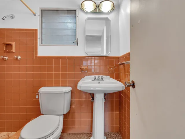 Terracotta-toned wall tiling featuring a built-in soap dish, a white pedestal sink, and a mirrored medicine cabinet with overhead lighting
