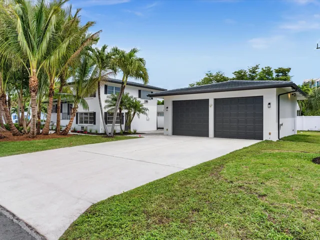 Dual-bay garage with modern doors, expansive concrete driveway, stucco exterior, and mature palm tree landscaping