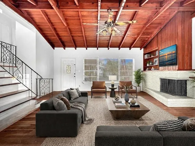 Vaulted wood-paneled ceiling with exposed beams, wood-finish flooring, white brick fireplace with built-in shelving, and an ornate wrought iron staircase