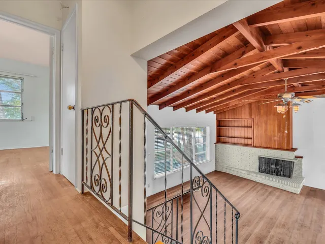 Vaulted wood-beam ceiling, wood-finish flooring, wrought iron staircase railing, built-in shelving, and a brick fireplace