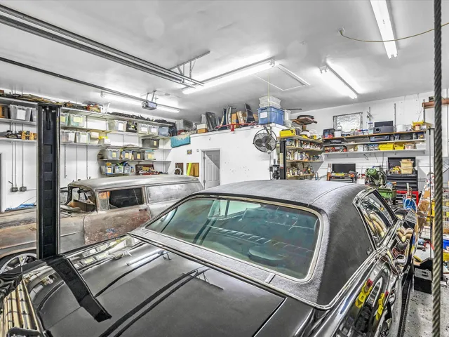 Garage space featuring a vehicle lift, extensive wall-mounted shelving, built-in overhead lighting, and a utility door