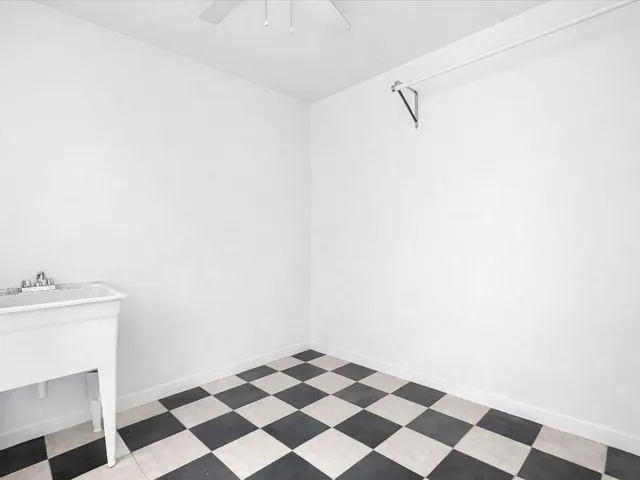 White utility sink, checkerboard flooring, ceiling-mounted fan, and wall-mounted drying rod