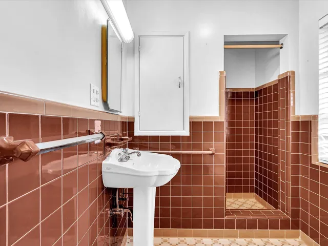 Pedestal sink, wall-mounted medicine cabinet, brown tiled walls, tiled shower stall, and patterned tile flooring