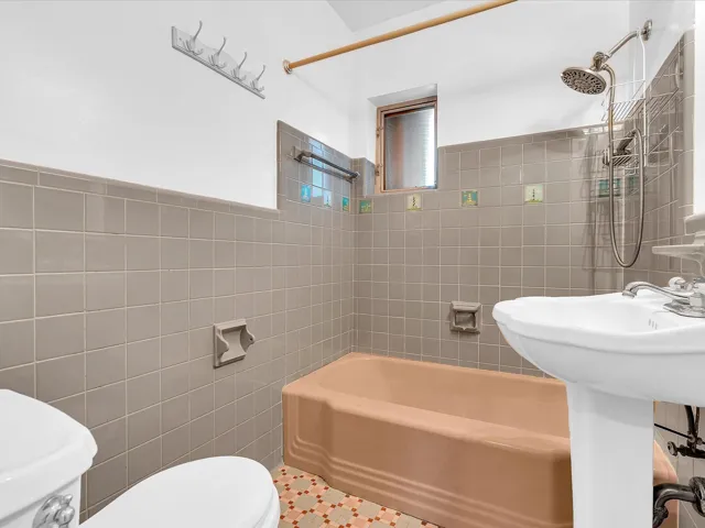 Pedestal sink with chrome fixtures, tiled walls, and a window for natural light