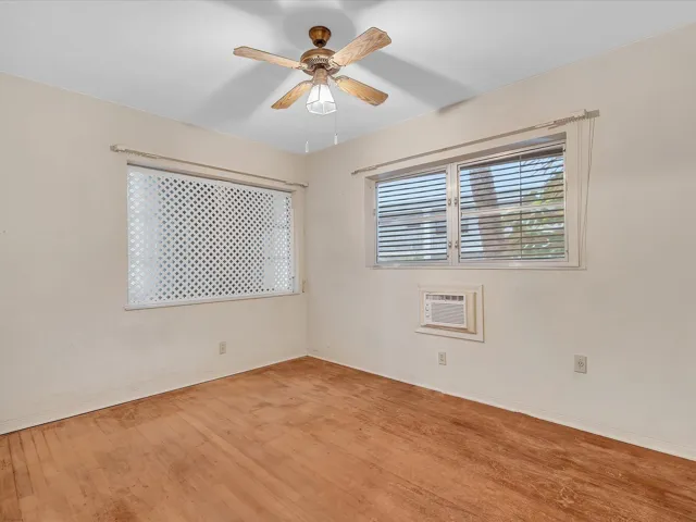 Wood-finish flooring with white walls, two windows with blinds, and a ceiling fan with integrated lighting