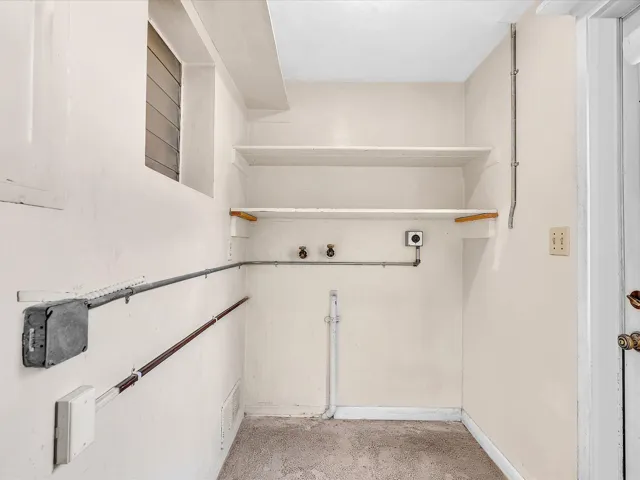 Utility space featuring two wall-mounted shelves, a louvered window, and exposed conduit