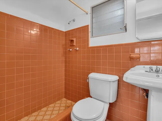Terracotta-toned tiled walls, pedestal sink, shower with tiled floor, and a louvered window