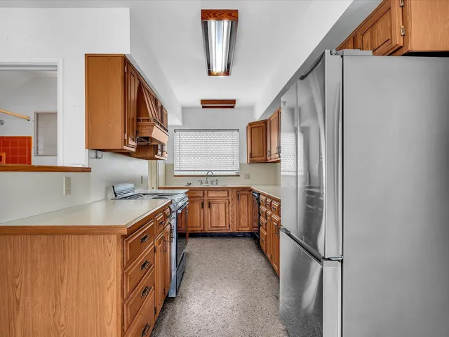 Galley kitchen featuring wood cabinetry, light-toned countertops, and stainless steel appliances