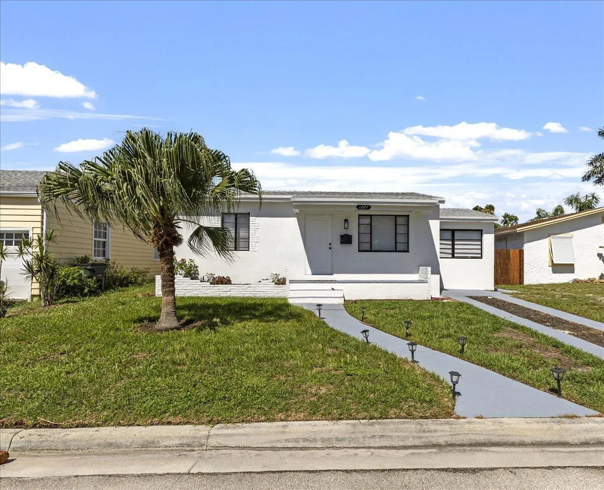 White exterior with black-trimmed windows, a palm tree, a front porch, and a paved driveway with integrated path lighting