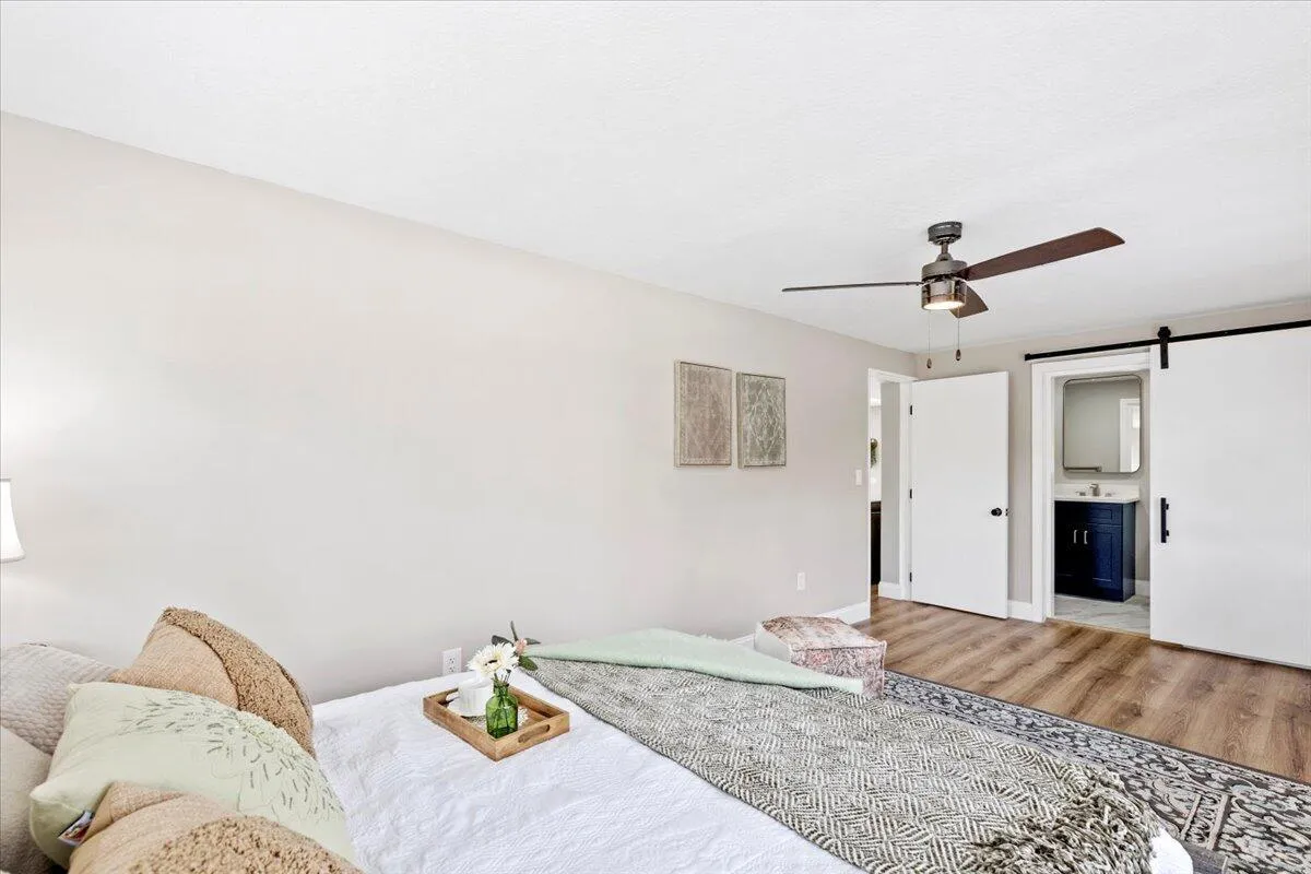 Wood-finish flooring, ceiling fan with light fixture, and barn door access to a bathroom featuring a vanity with an integrated sink