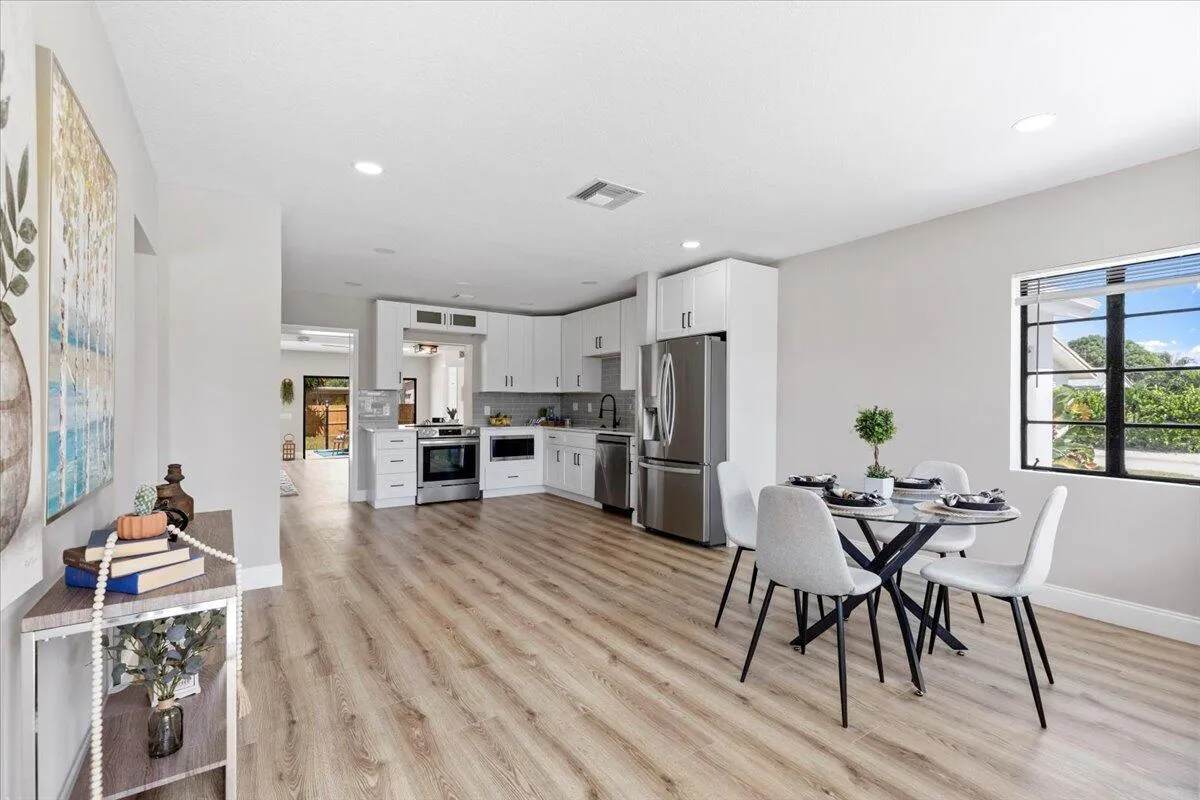 Open-concept living space with wood-finish flooring, white cabinetry, stainless steel appliances, recessed lighting, and a large window
