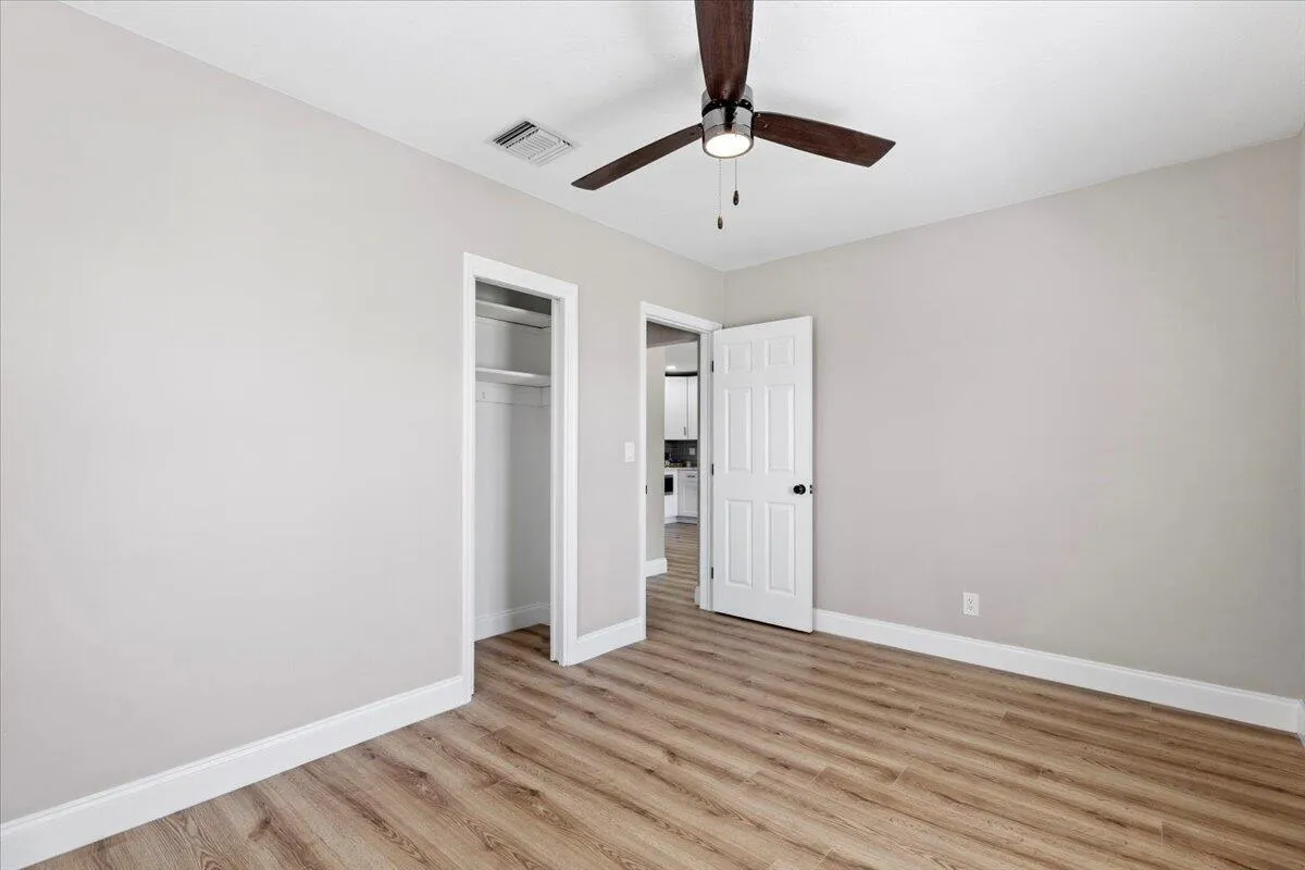 Wood-finish flooring, light neutral wall paint, white trim, ceiling fan with integrated lighting, and an open closet with shelving