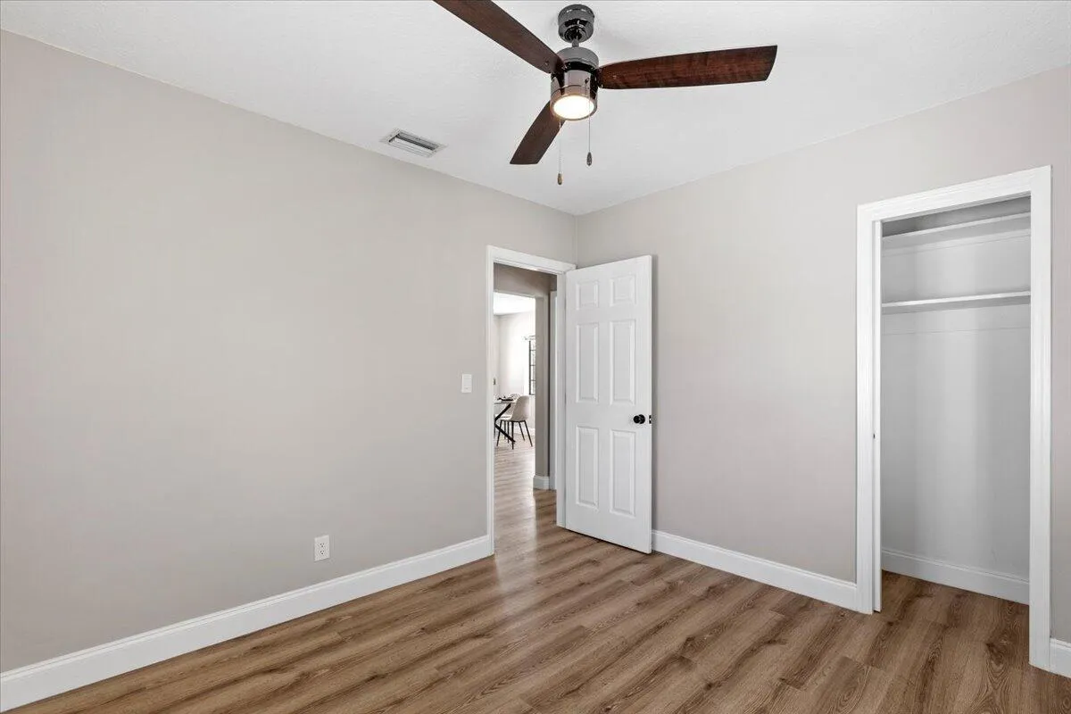 Wood-finish flooring, light neutral wall paint, white trim, ceiling fan, and a built-in closet with shelving
