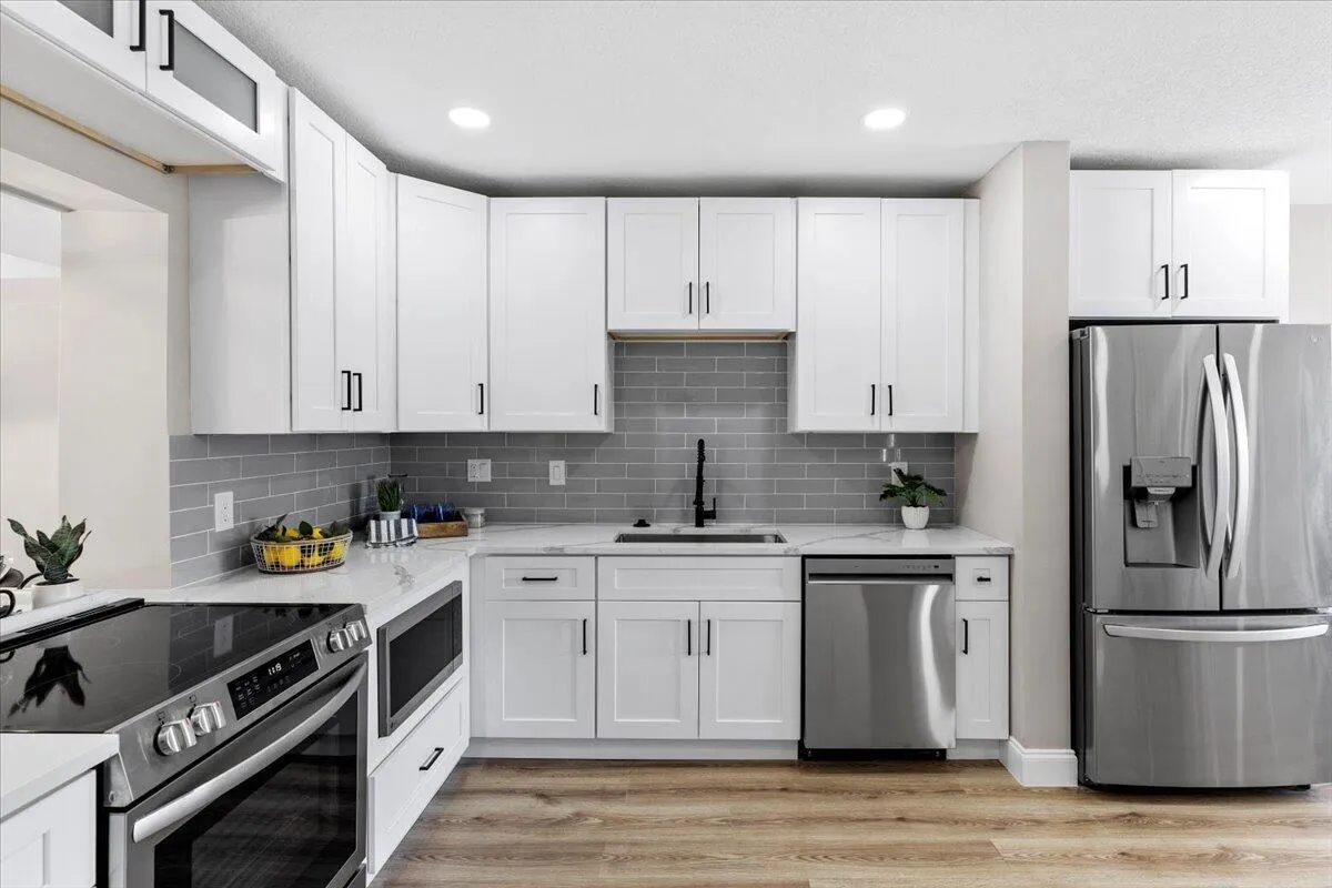 White shaker-style cabinetry with matte black hardware, stainless steel appliances, a subway tile backsplash, and wood-finish flooring