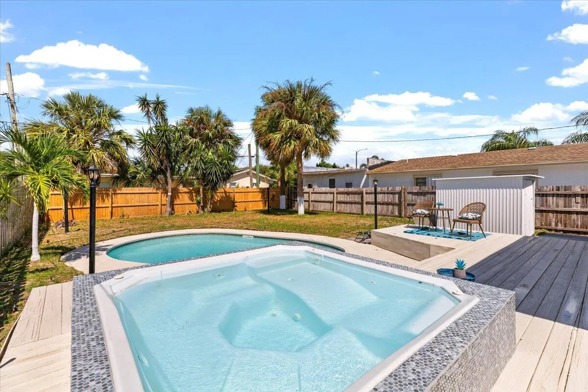 Outdoor spa and swimming pool with surrounding wood-finish decking and privacy fencing