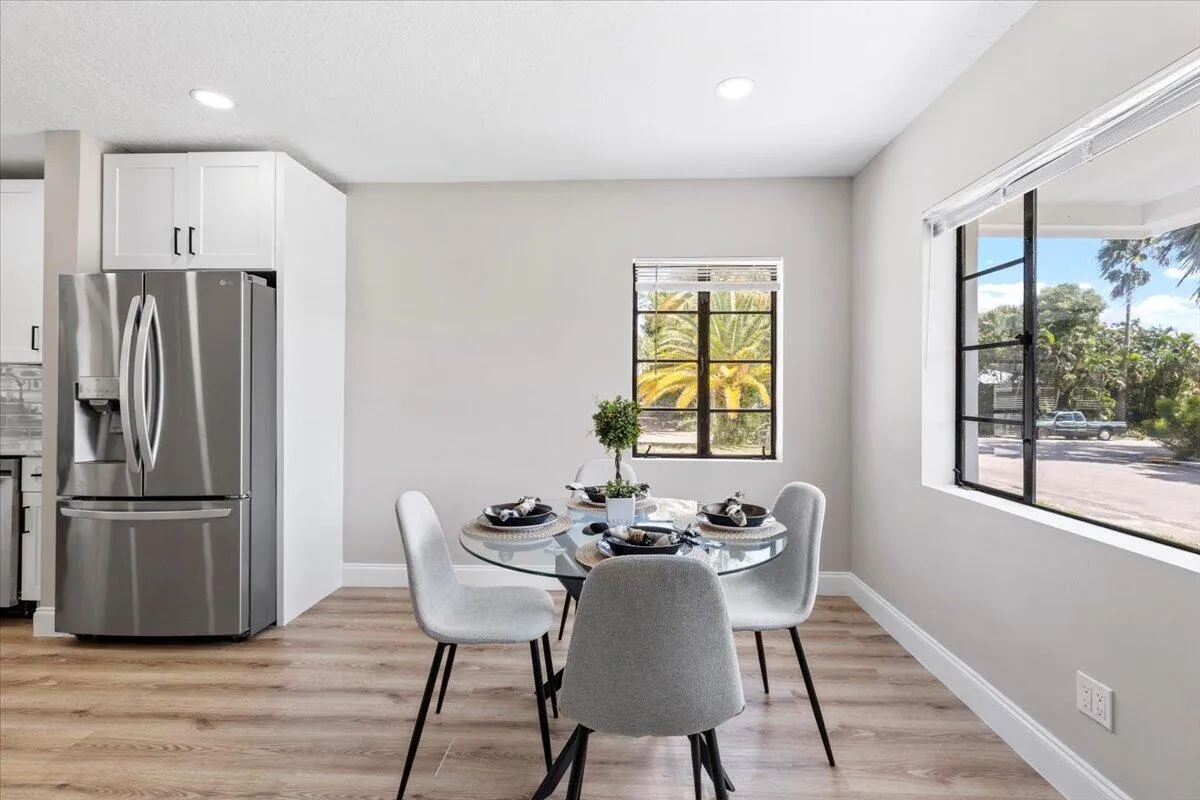 Recessed ceiling lighting, wood-finish flooring, white cabinetry, stainless steel refrigerator, and black-framed windows