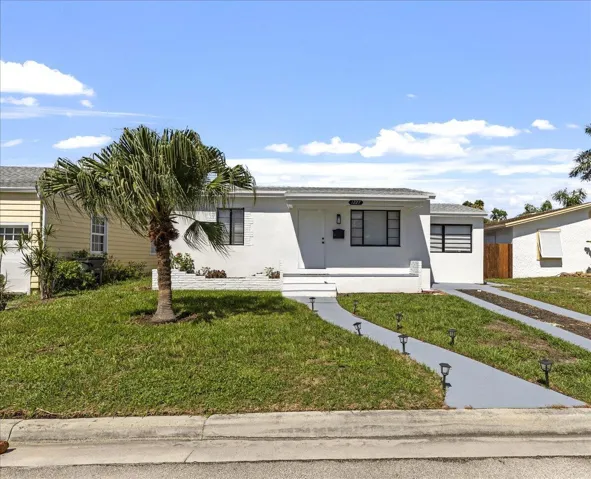 White exterior with black-trimmed windows, a palm tree, a front porch, and a paved driveway with integrated path lighting