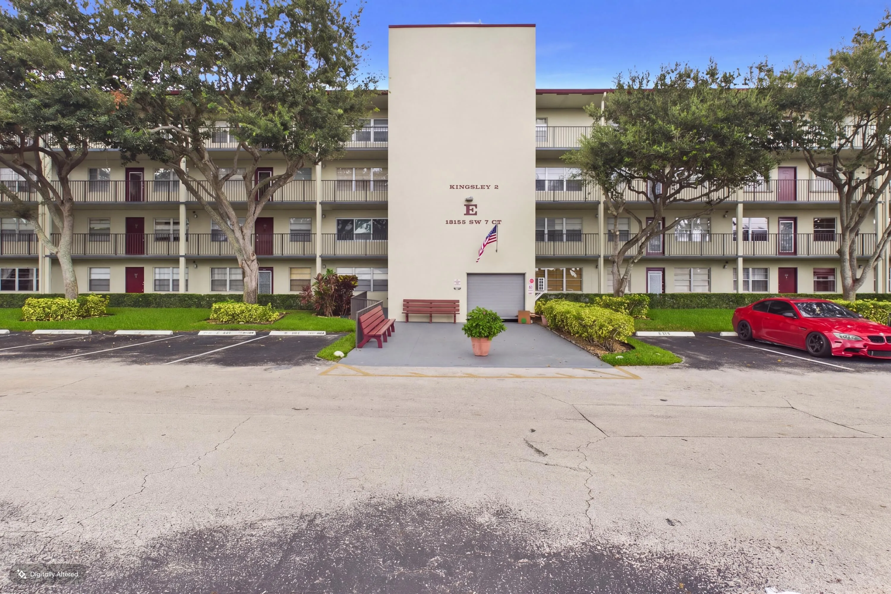 Multi-story residential building with multiple balconies, an integrated central entrance, and a surrounding parking area