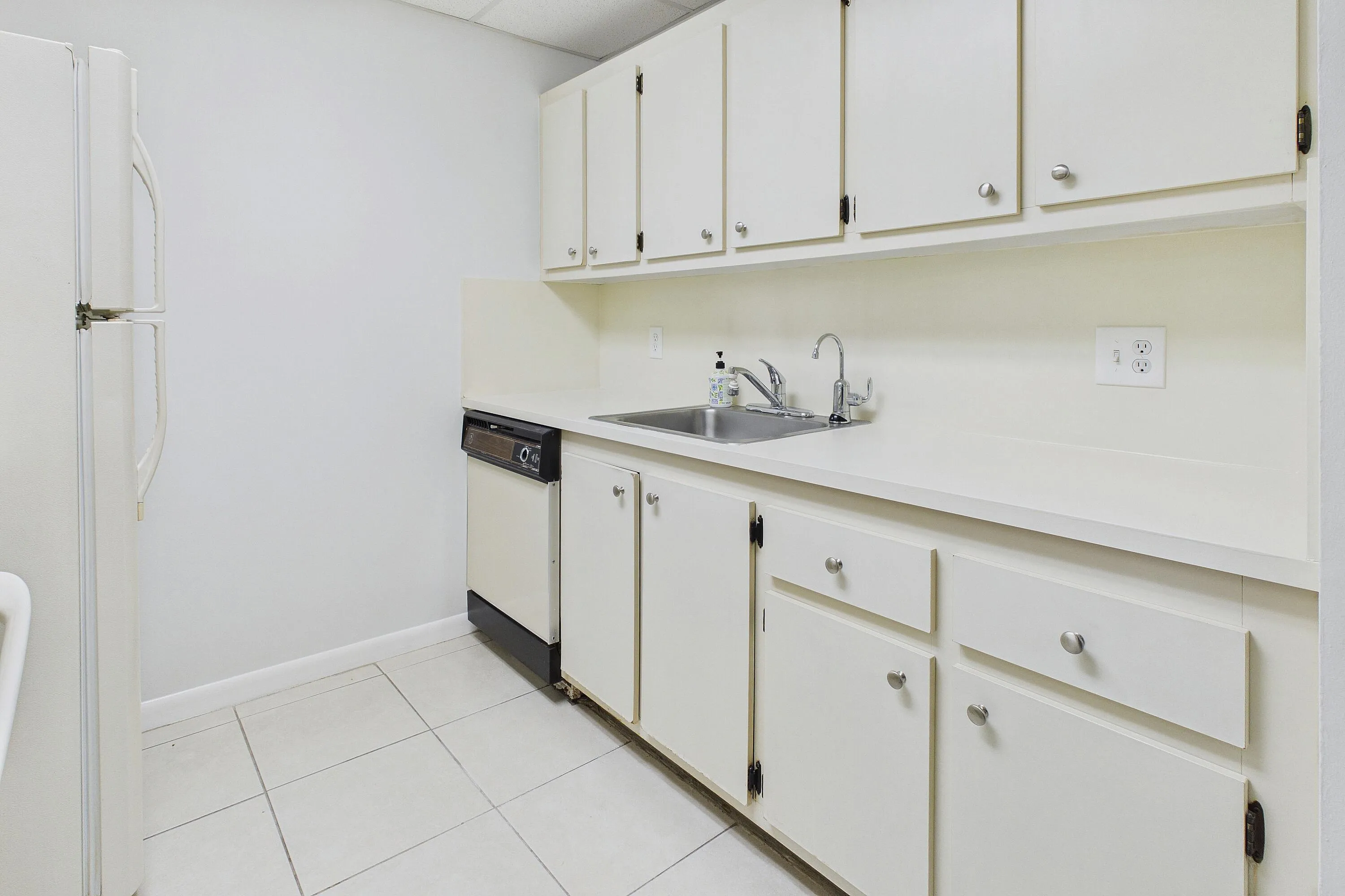 White cabinetry with chrome hardware, an integrated stainless steel sink, a dishwasher, and a​​‌​​​​‌​​‌‌​‌‌​​​‌‌​‌​‌​‌​​​‌​​ refrigerator