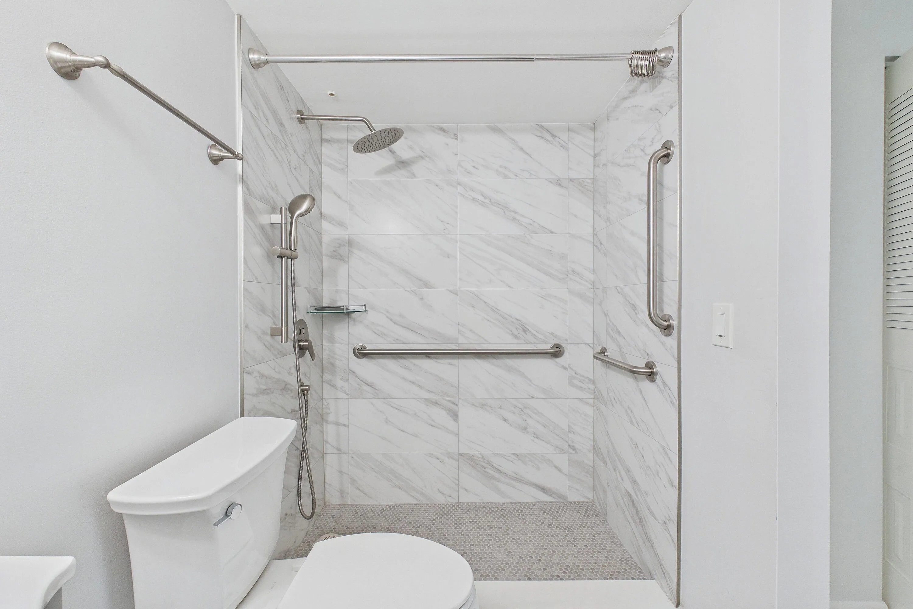 Renovated handicap accessible walk-in shower featuring marble-look wall tiles, a rainfall showerhead, and a handheld shower fixture