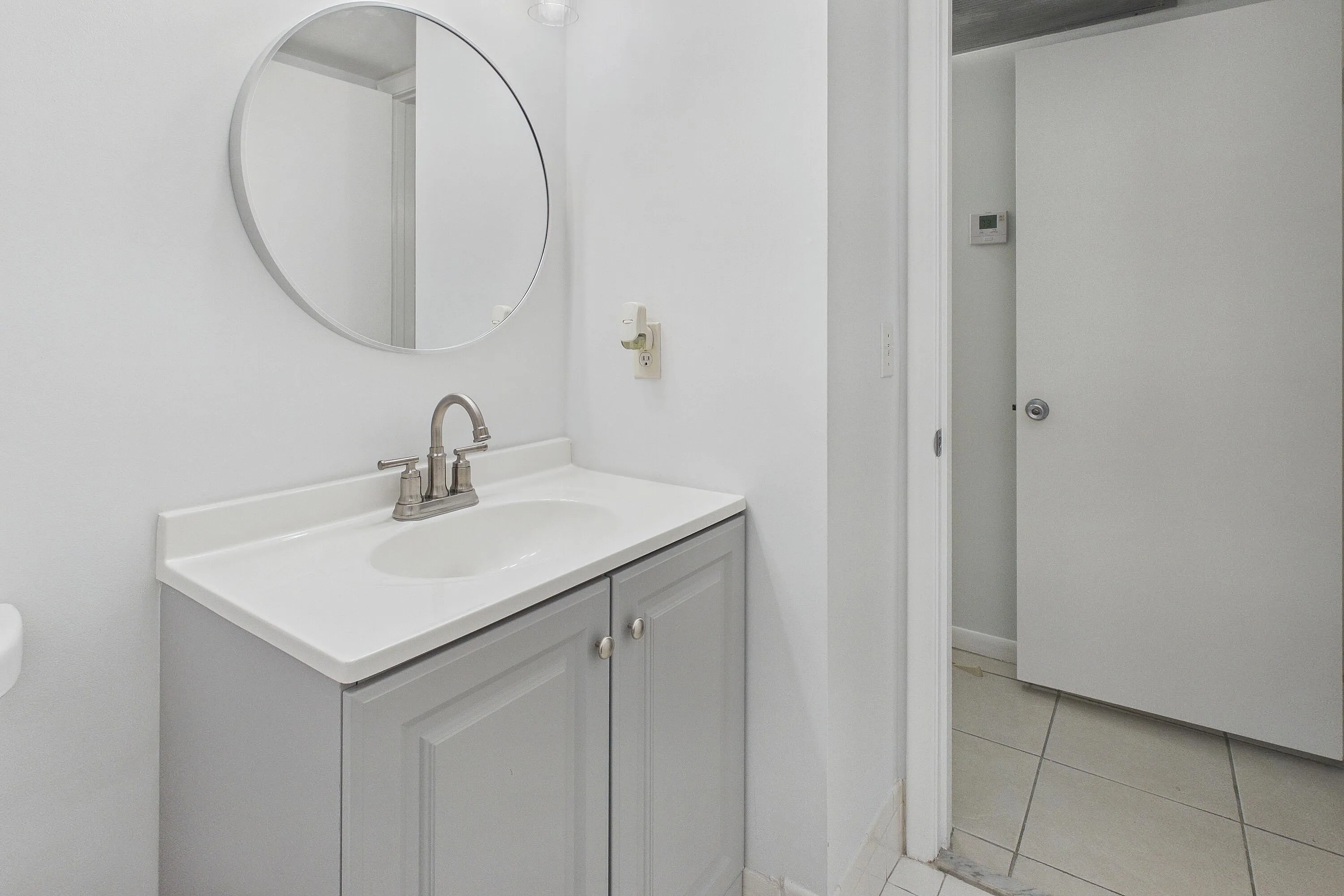 White vanity with a single basin sink, brushed nickel faucet, and a circular wall-mounted mirror