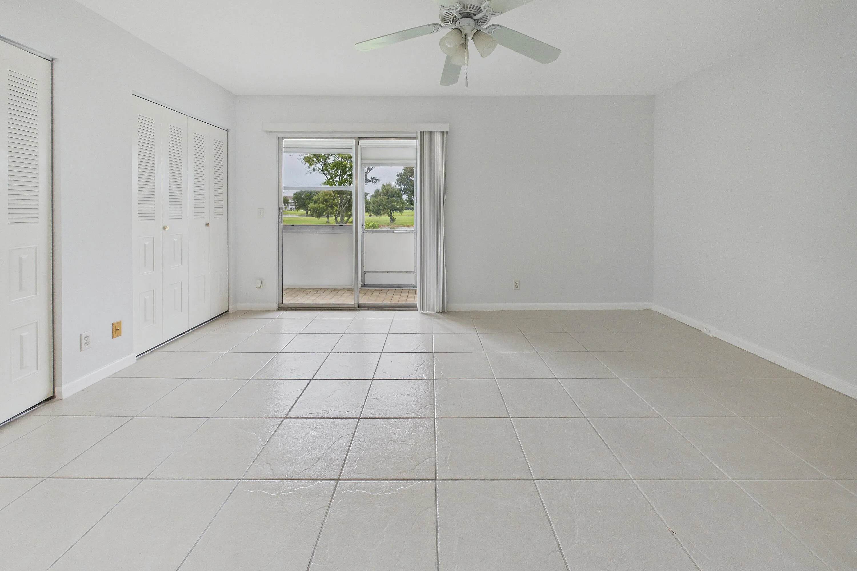Neutral tile flooring, white walls, louvered closet doors, ceiling fan, and sliding glass door with outdoor access