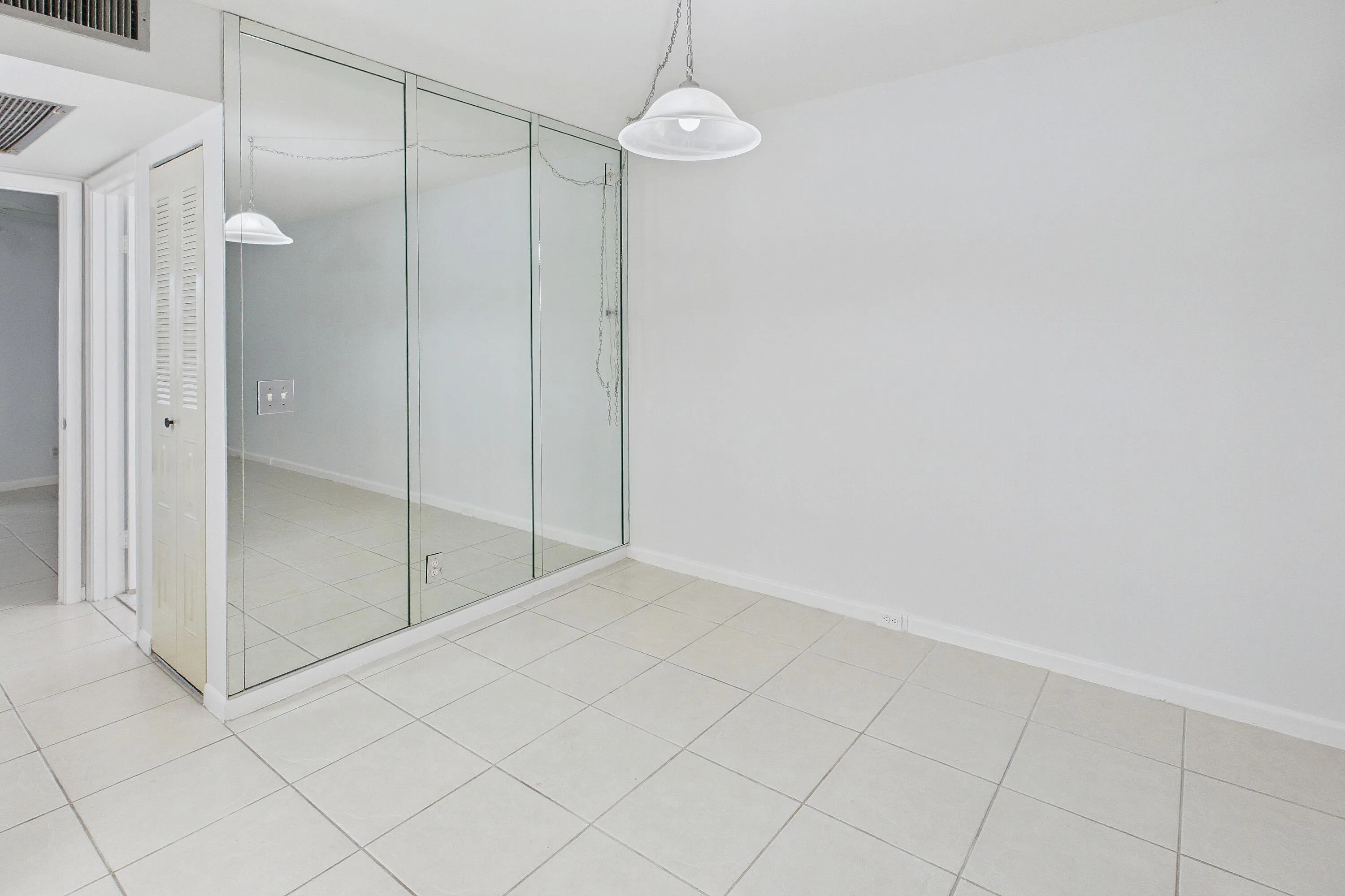 Tile flooring, mirrored wall, white walls, and a ceiling-mounted light fixture.