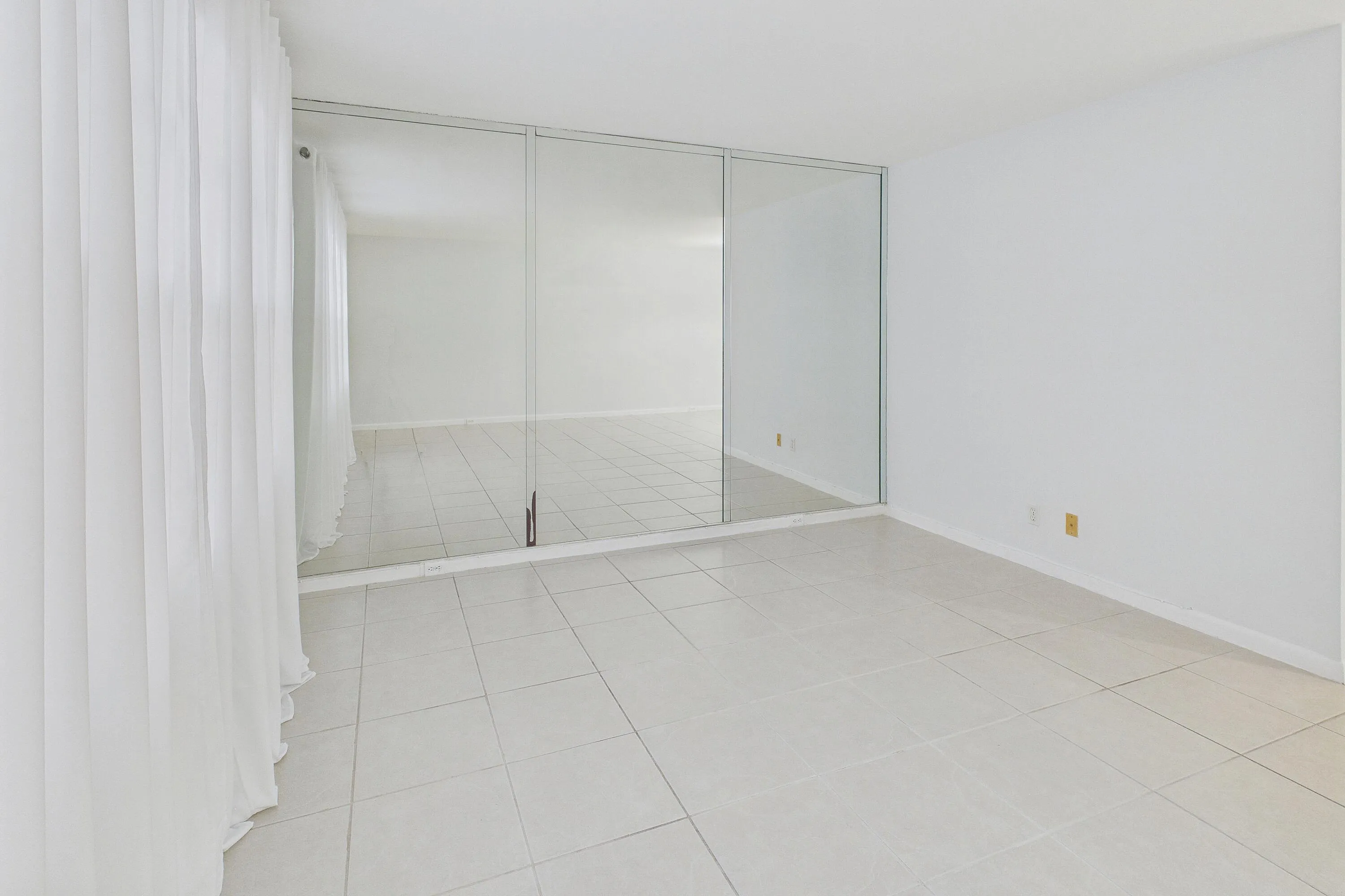 White tile flooring, full-height mirrored wall, and sheer white curtains.