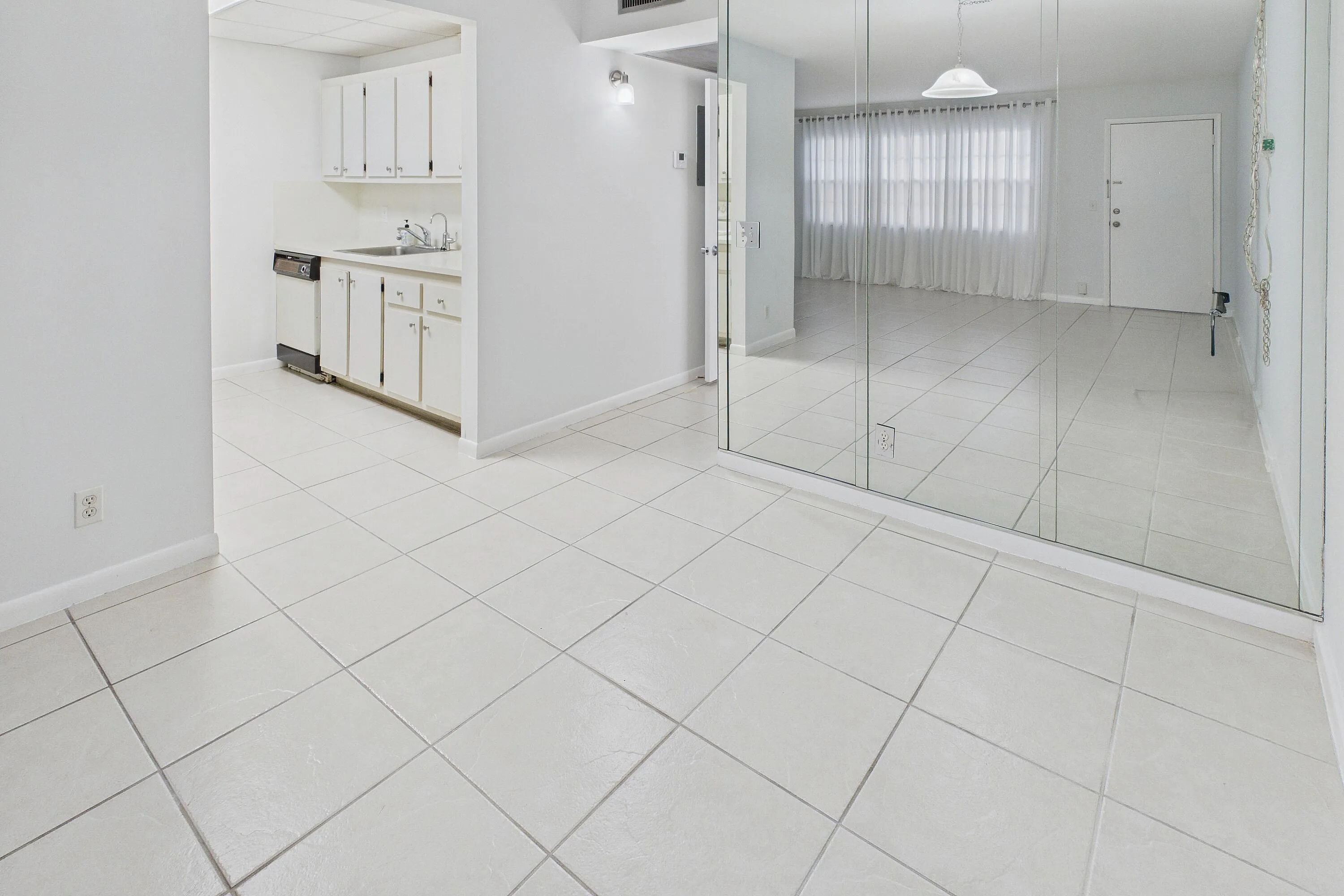 Ceramic tile flooring throughout, white cabinetry, dishwasher, and full-wall mirrored accents.