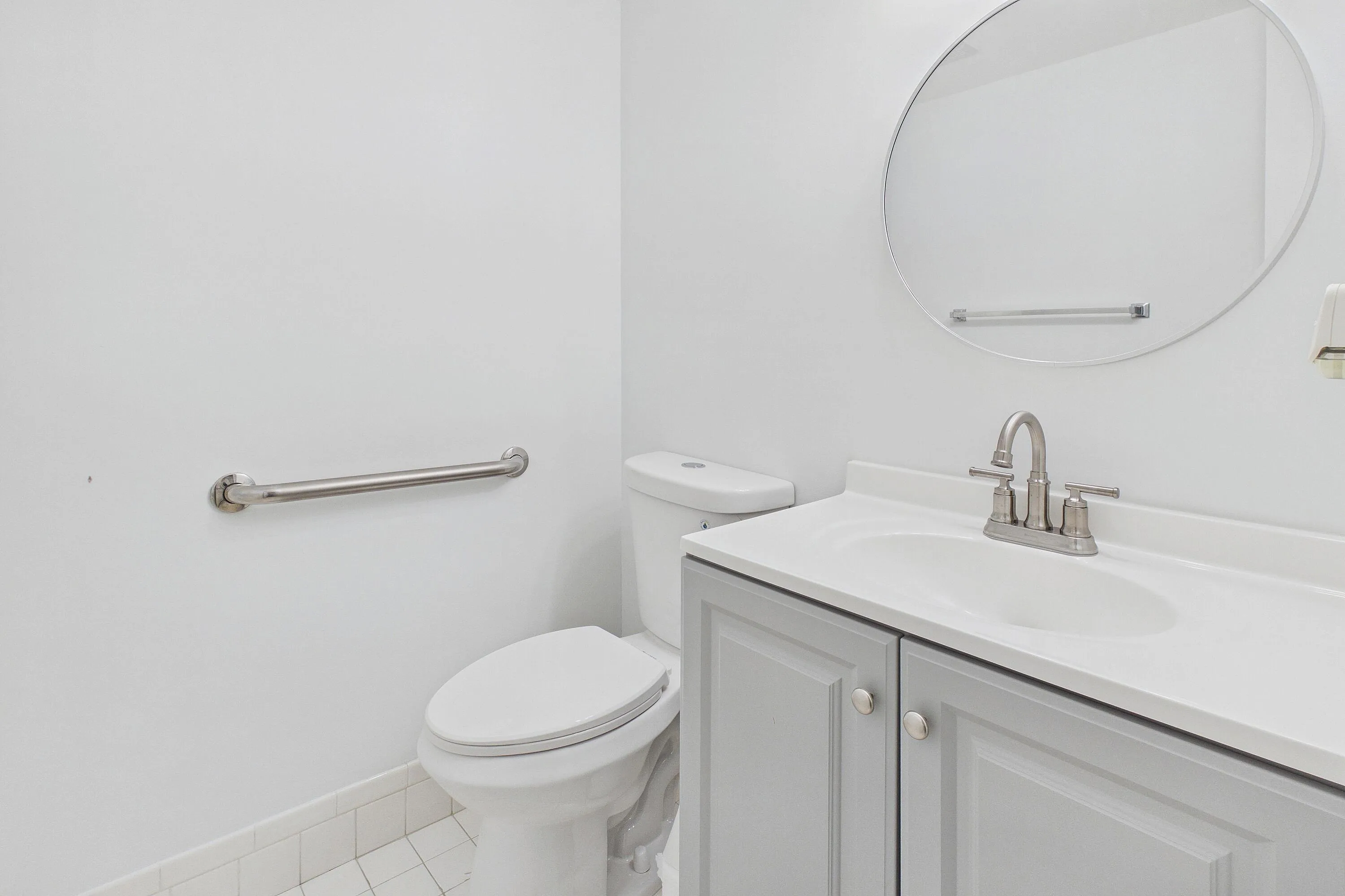Bathroom featuring a vanity with a light gray cabinet, white countertop, integrated sink, and a circular mirror