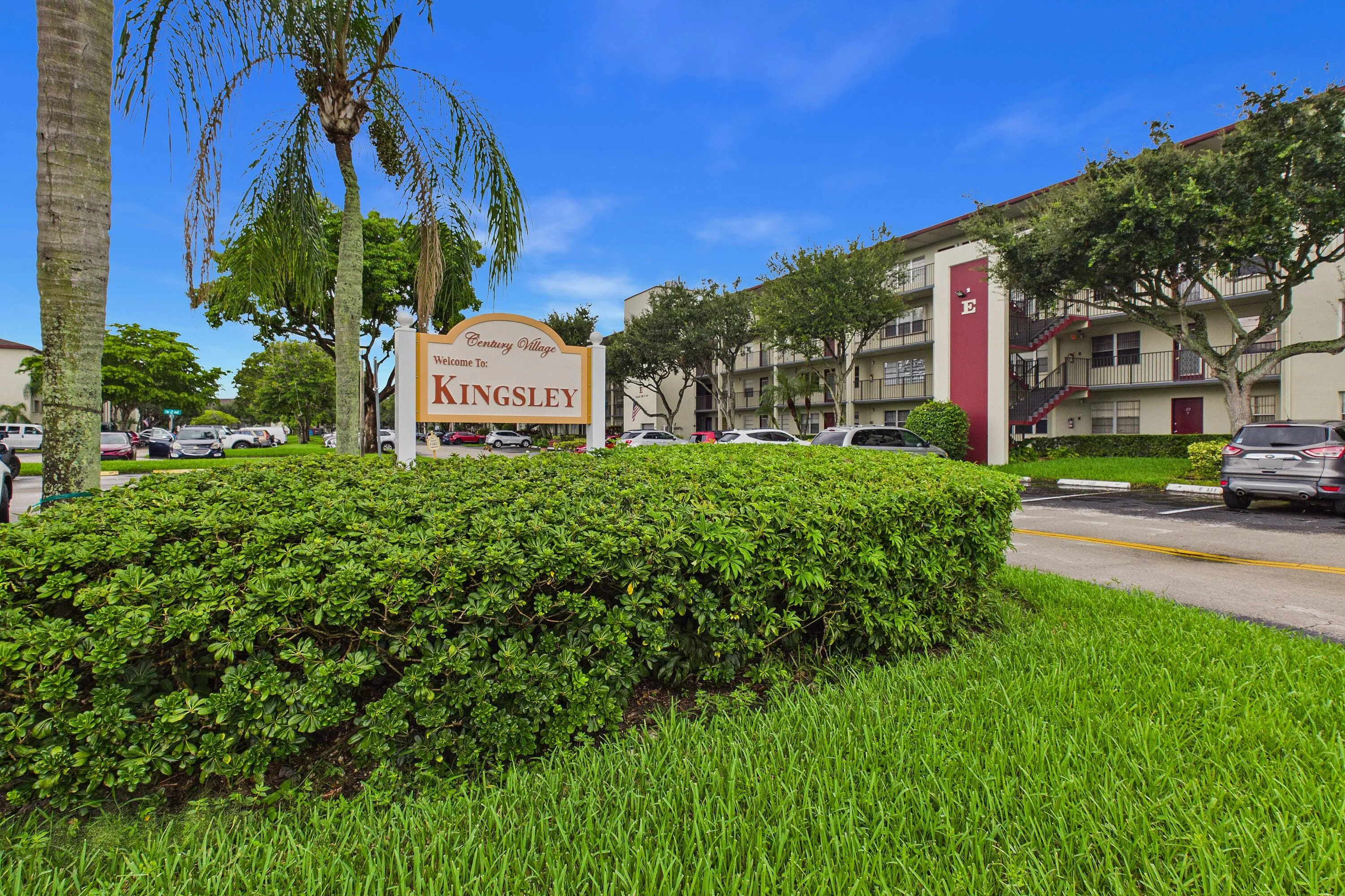 Building exterior with balconies, a prominent entrance sign, and mature landscaping