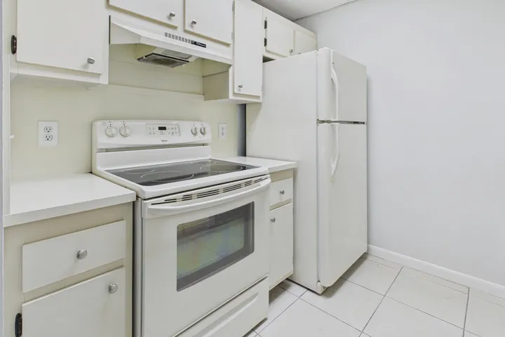 Kitchen featuring white cabinetry, solid surface countertops, white refrigerator, electric range, and tiled flooring