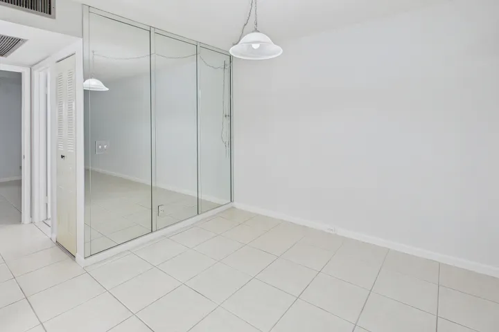 Tile flooring, mirrored wall, white walls, and a ceiling-mounted light fixture.