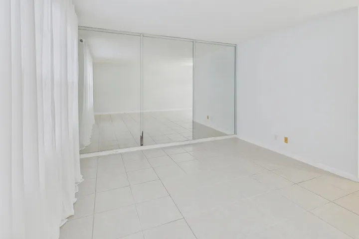 White tile flooring, full-height mirrored wall, and sheer white curtains.