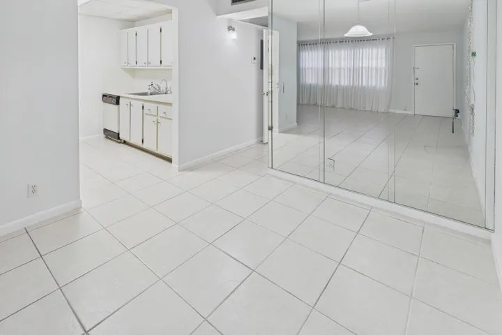 Ceramic tile flooring throughout, white cabinetry, dishwasher, and full-wall mirrored accents.